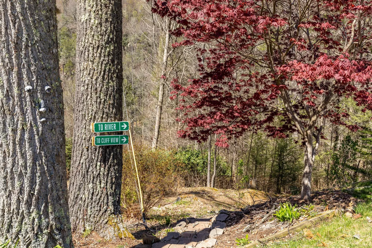 A scenic exterior shot featuring a signpost, a vibrant red tree, and a stone pathway leading off into the woods—an invitation to nature walks and exploration right from the doorstep.