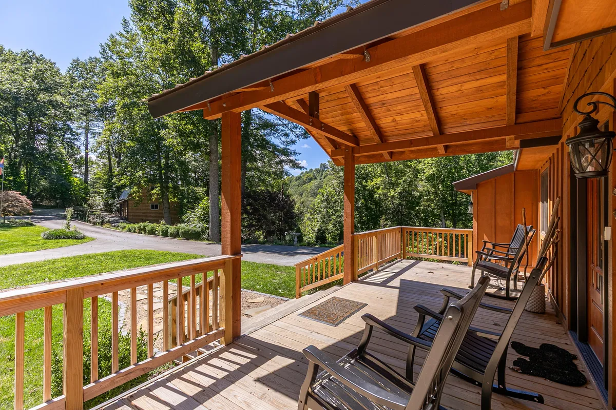 A wooden porch with classic rocking chairs overlooks a lush green landscape. Wooden beams and rustic details frame the view, inviting guests to relax and soak in the mountain scenery or enjoy peaceful moments outdoors.