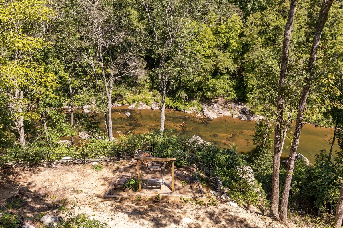 A swing seat is positioned by the river, surrounded by trees, offering a peaceful spot for relaxation or nature observation. The river glimmers in the light, emphasizing quiet riverside moments.