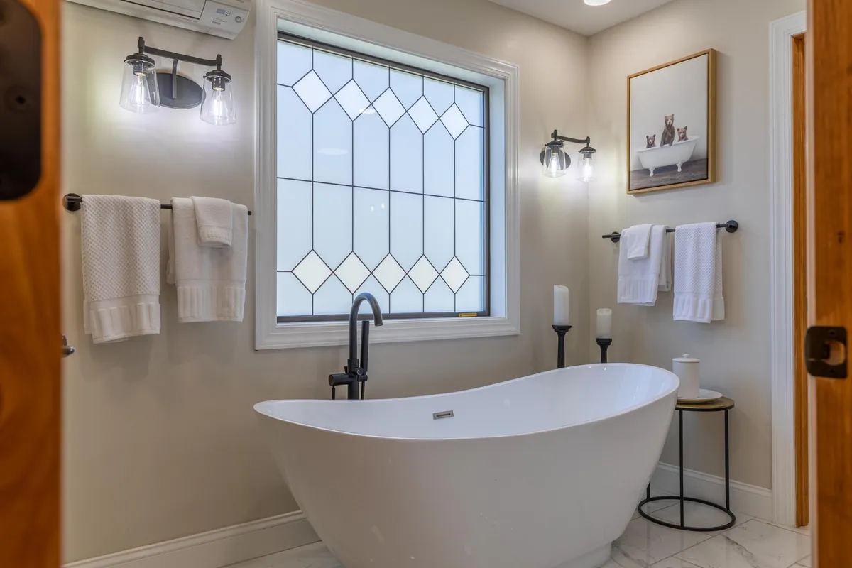 A serene bathroom with a freestanding bathtub beneath a stained glass window, complemented by wall art. The space exudes a spa-like atmosphere, perfect for relaxation and rejuvenation.