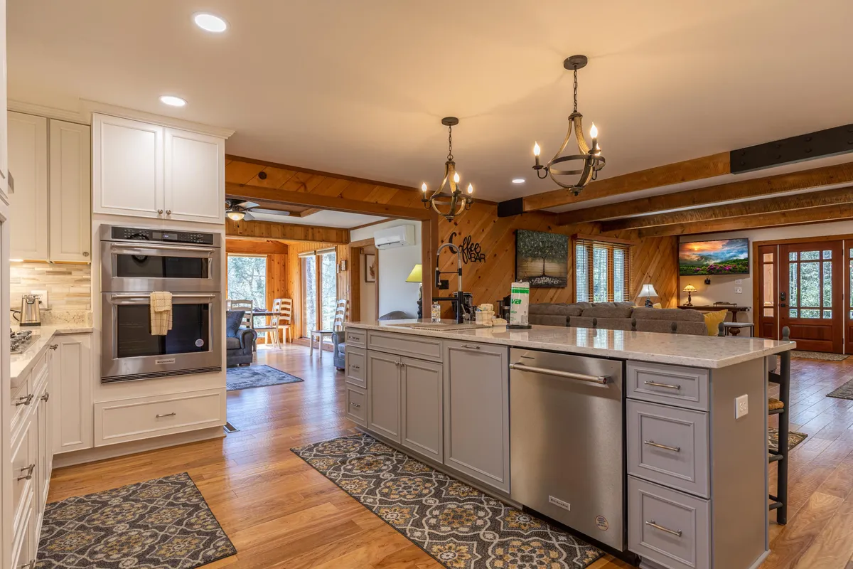 An open-concept kitchen with a spacious island countertop, modern oven, decorative chandelier, and a clear view into the adjoining living area. The setting is warm and welcoming, ideal for both casual and festive occasions.