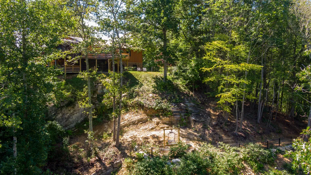 A spacious wooden deck overlooks lush greenery, with a natural stone path leading into the yard and a swing set nestled by the trees. The outdoor area is inviting and versatile, offering spaces for both relaxation and playtime.