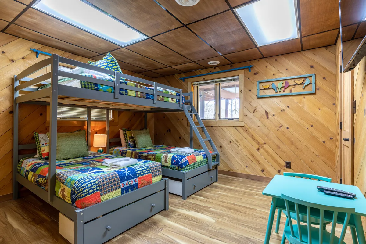 A cheerful bunkroom with custom-built bunk beds dressed in colorful quilts, a small green table, and playful accents. The space is designed to delight younger guests or families and offers a cozy, fun environment.